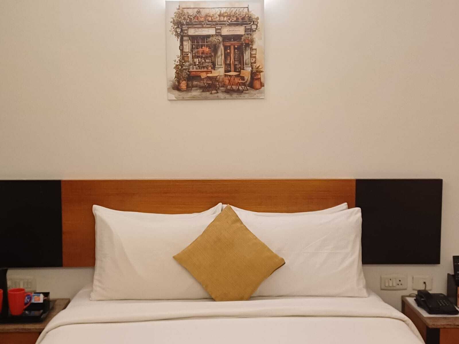 A hotel room with a bed, a nightstand with a phone, and a wall-mounted painting.