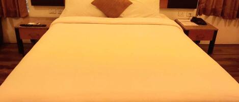 A hotel room with a large bed, two bedside tables, a remote control, and a telephone on one of the tables.