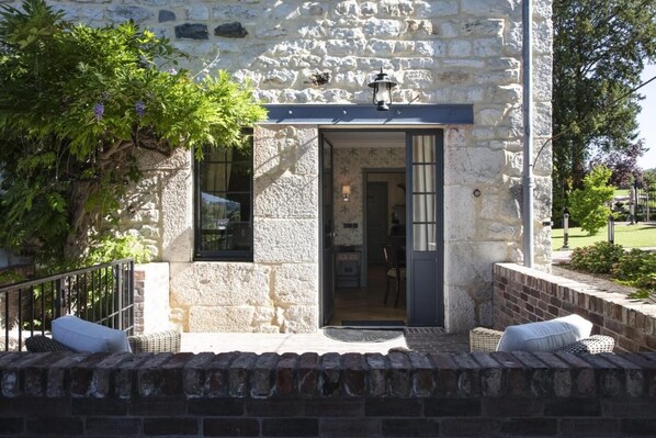 A stone building with a wooden door, a small porch with wicker furniture, and a tree with purple flowers. - Château Brachet  (Gresy-sur-Aix)