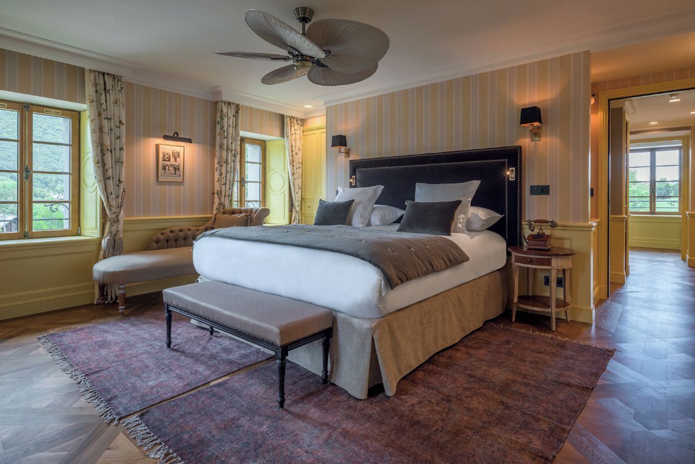 A large bed with a dark headboard, a bench, and a bedside table with a lamp.