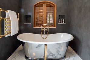 A freestanding bathtub with a marble finish, a gold faucet, and a wooden window with blinds. - Château Brachet  (Gresy-sur-Aix)