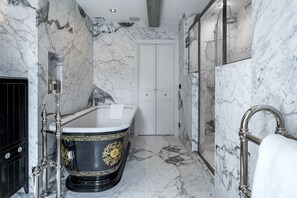 A luxurious bathroom with a marble floor, a freestanding bathtub with gold floral designs, a glass-enclosed shower, and a white double door. - Château Brachet  (Gresy-sur-Aix)