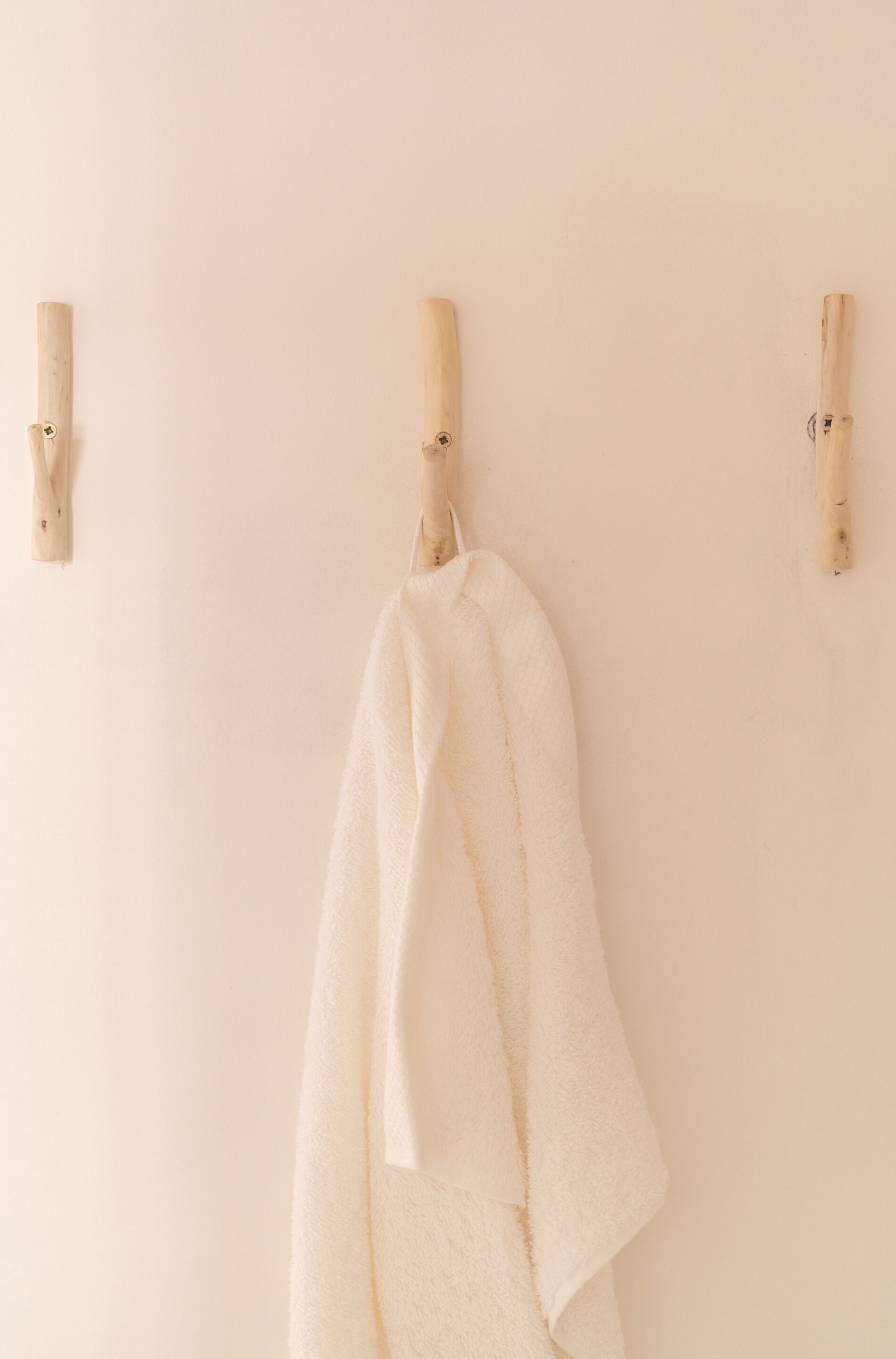Une serviette blanche est suspendue à un porte-serviettes en bois, devant un mur uni.
