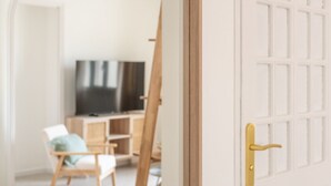 Een kamer met een witte deur, een televisie, een stoel en een houten schilderstandaard.