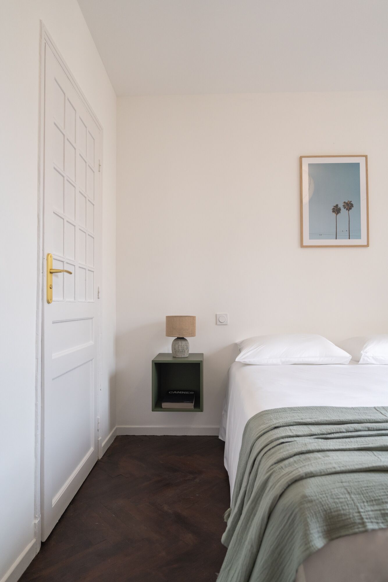 Een slaapkamer met een bed, een nachtkastje met een lamp, een ingelijste foto aan de muur en een deur.