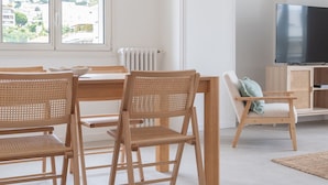 Een moderne woonkamer met een eethoek, met houten meubels, een groot raam en een televisie.