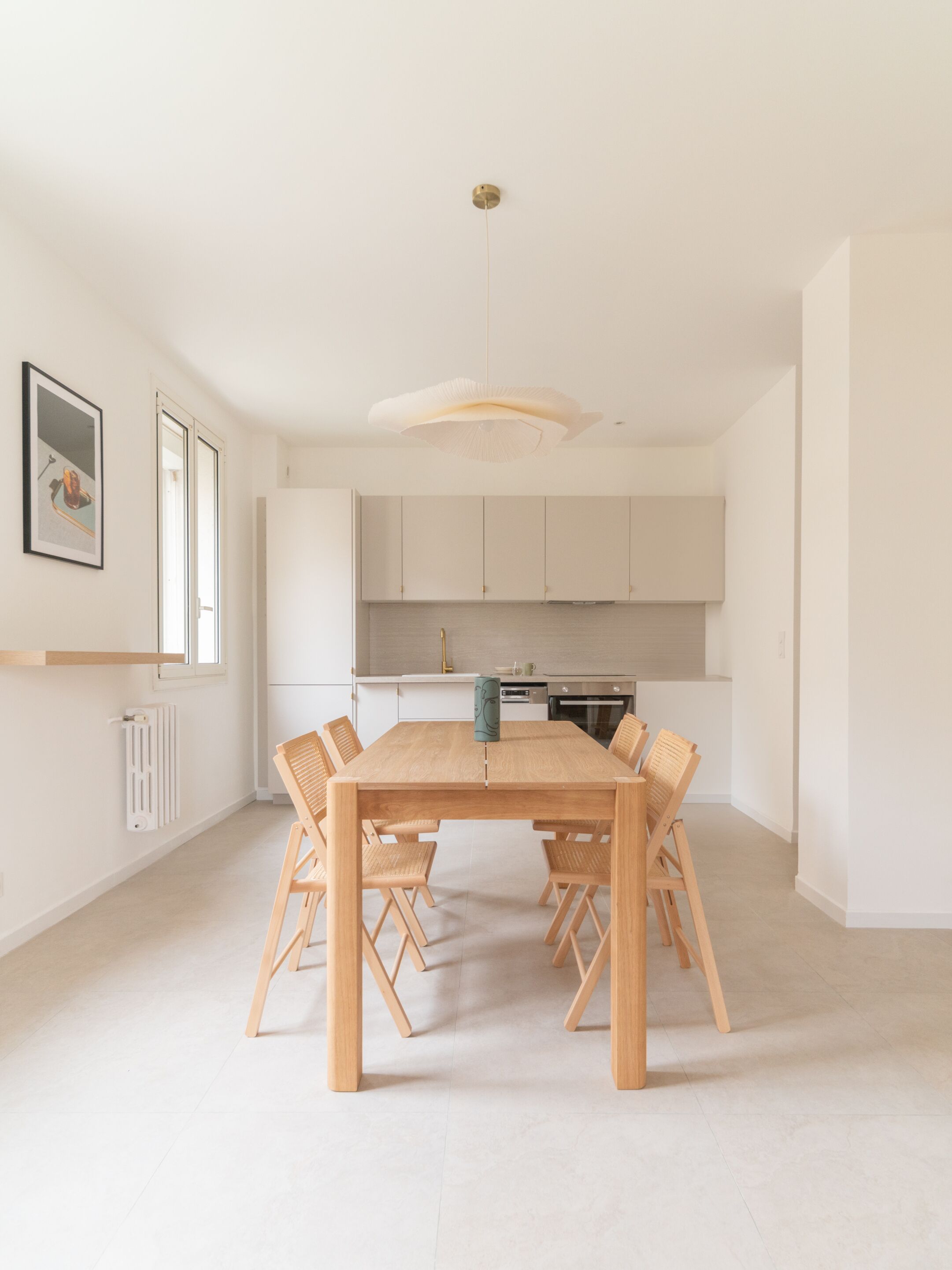 Una cocina moderna con armarios blancos, una mesa de comedor de madera y una lámpara colgante.