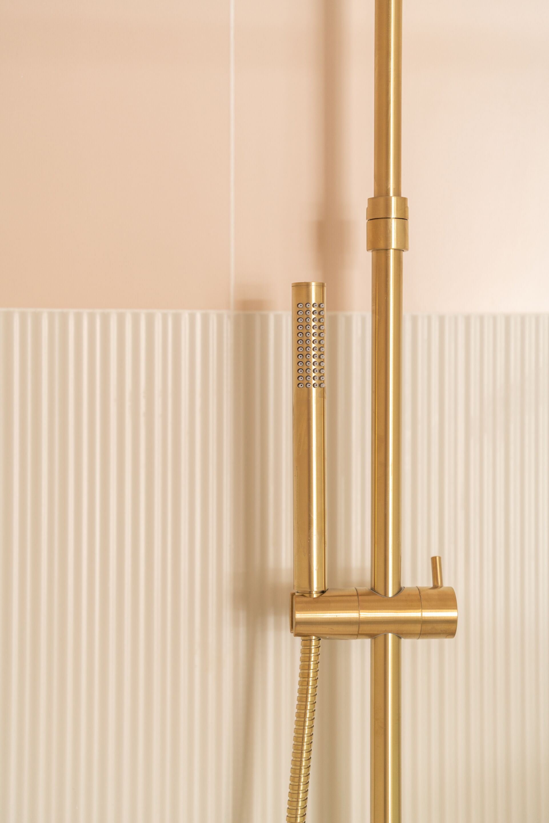Un pommeau de douche de couleur dorée, doté d’un flexible, est fixé sur un mur à texture.