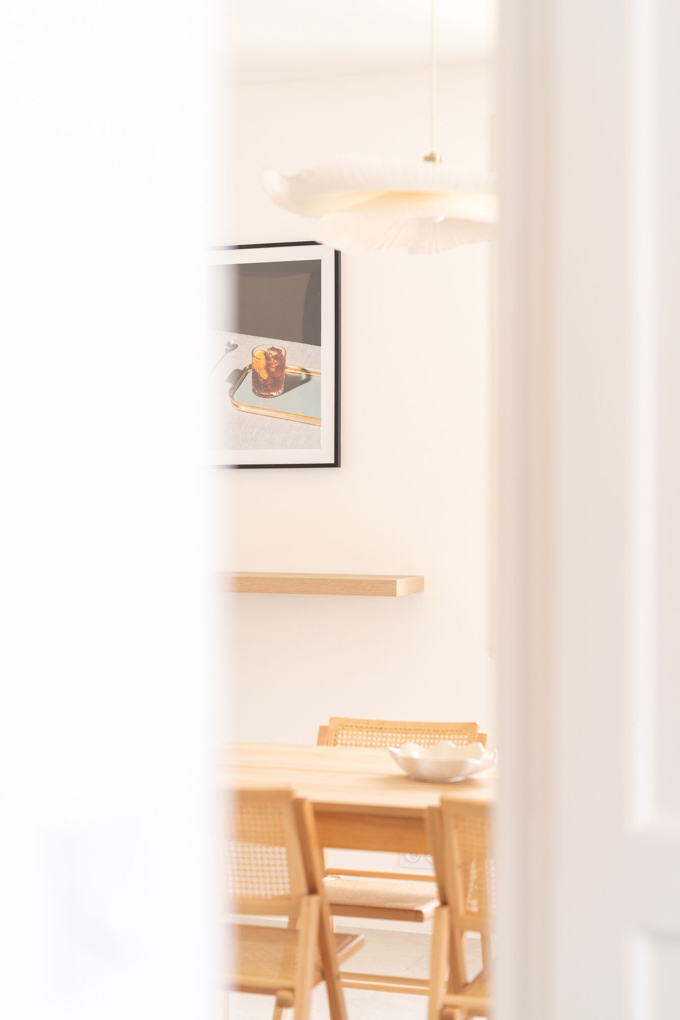 A bright, minimalist dining area with a wooden table, chairs, and a hanging light fixture.