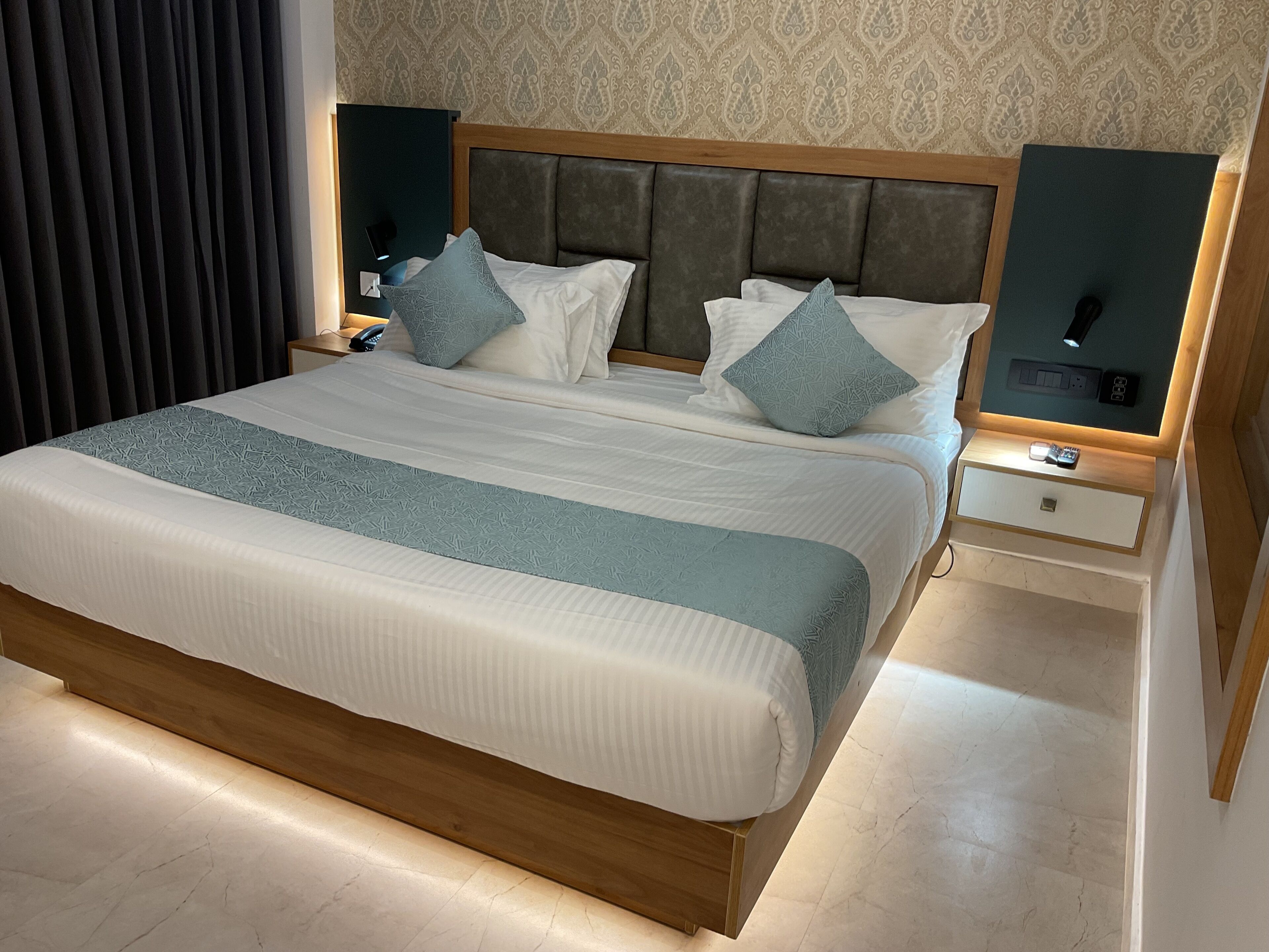 A hotel room with a large bed, two bedside tables, a nightstand, and a headboard with built-in lighting.