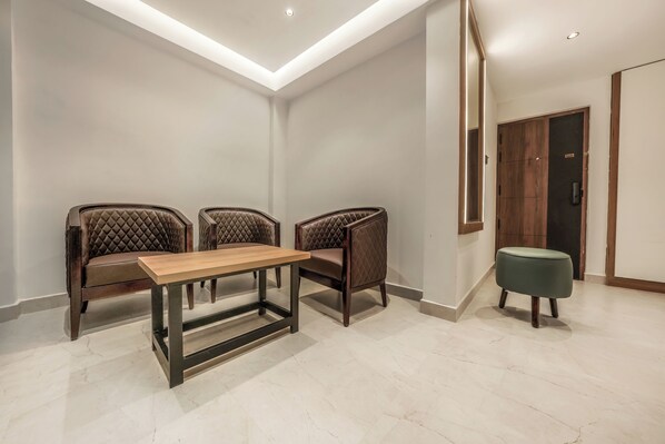 Een moderne kamer met een houten tafel en twee comfortabele stoelen, een groene poef, en een houten deur.