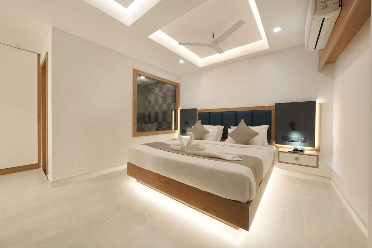 Une chambre à coucher moderne avec un grand lit, un ventilateur de plafond, un éclairage encastré et un téléviseur fixé au mur.