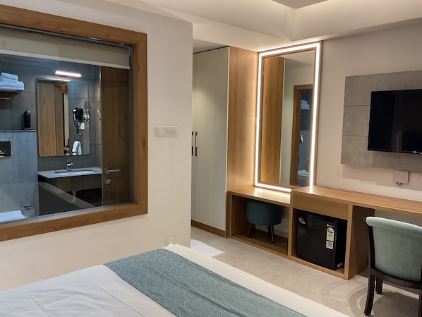 Una camera d'albergo moderna con un letto grande, una scrivania con uno specchio, una televisione e un piccolo frigorifero.