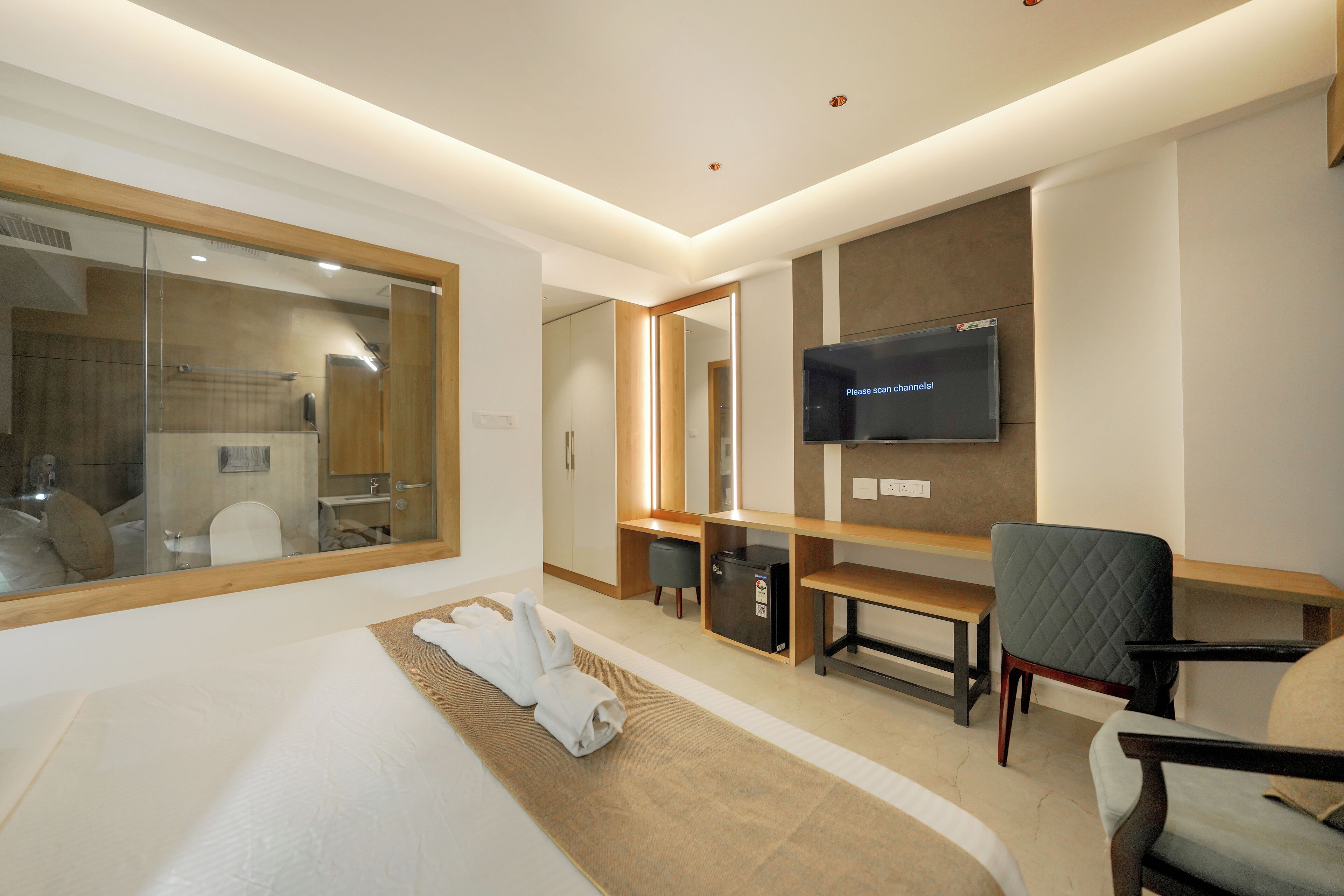 Quarto de hotel moderno com uma cama grande, televisão na parede, escrivaninha e uma cadeira.
