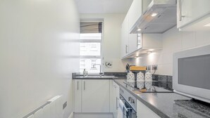 A modern kitchen with white cabinets, a granite countertop, a built-in oven, and a window providing natural light. - Iconic Oxford Street Apartment ✨ 2 Bed 1 Bath ✨ Tube ✨ Bond Street 📍 (Greater London)