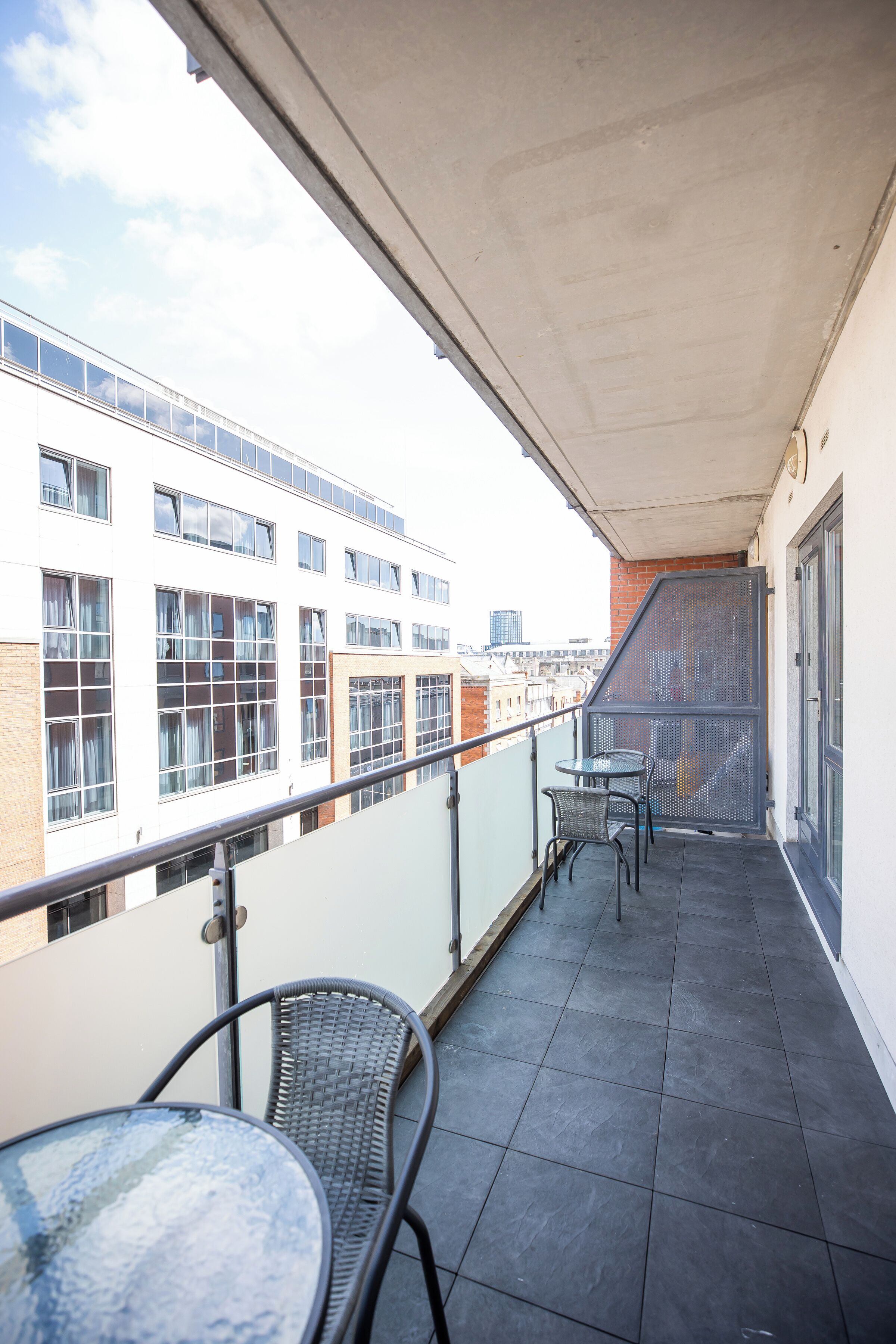 Un balcon doté d’une balustrade en verre, de deux tables et de chaises.