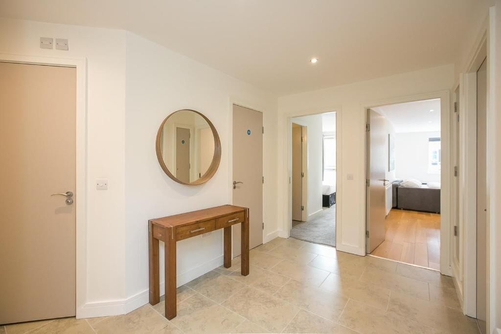A hallway with a wooden console table and a mirror, leading to a bedroom with a bed and a bathroom.