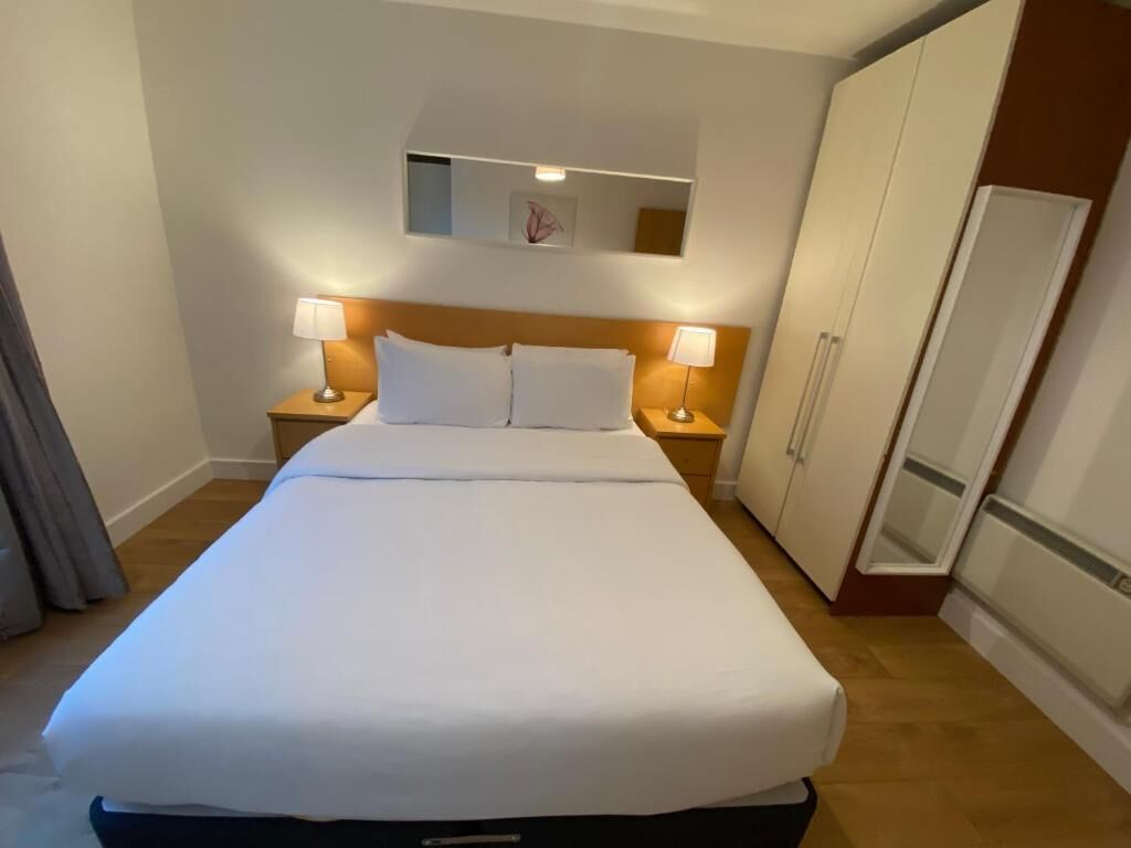 Et hotelværelse med en stor seng, to sengeborde med lamper, et skab og et køleskab.