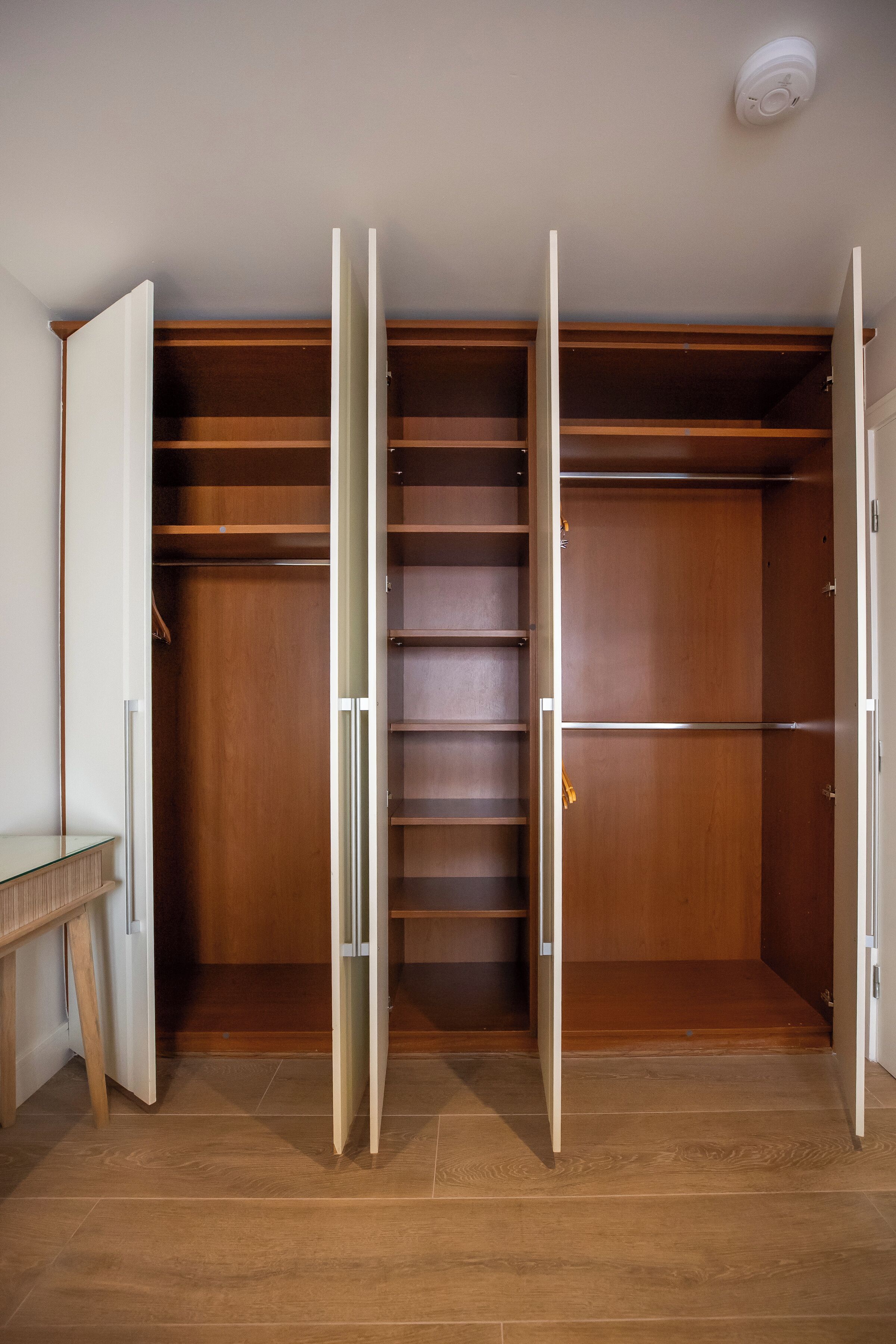 Un vestidor con puertas abiertas, estantes de madera y suelo de baldosas.