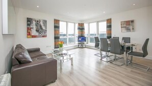 Ein modernes Wohnzimmer mit braunem Ledersofa, einem Glastisch und einem Essbereich mit Tisch und Stühlen.