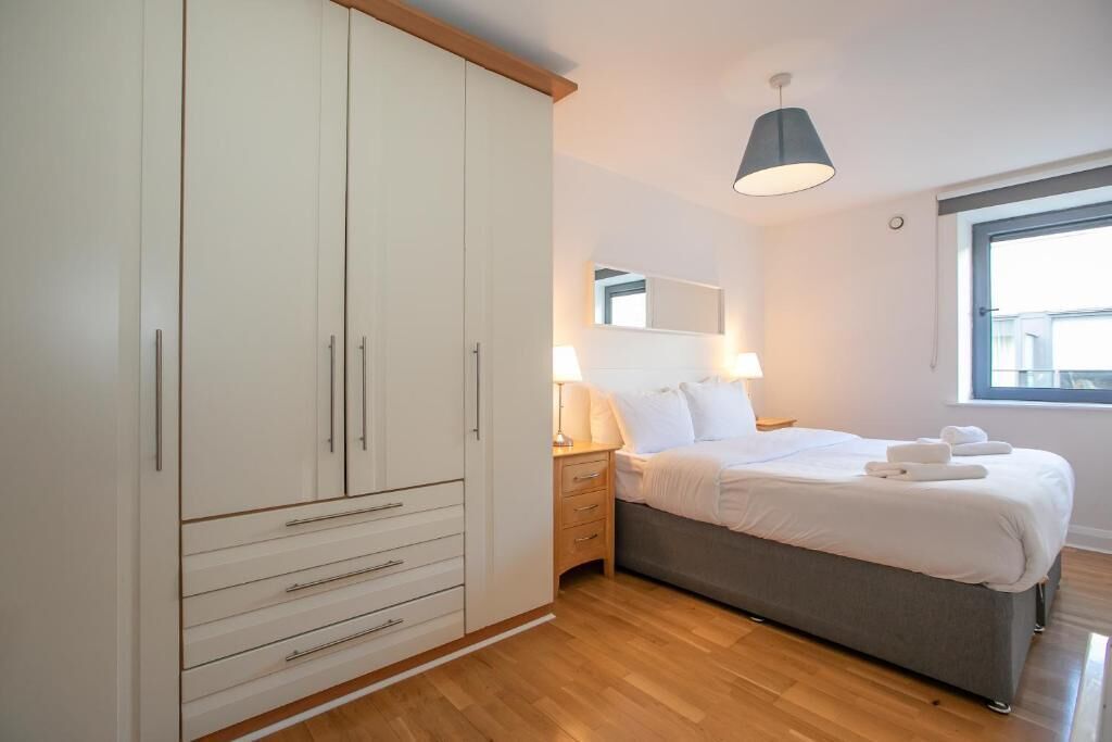 A bedroom with a bed, bedside lamps, a wardrobe, and a window.