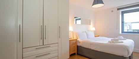A bedroom with a bed, bedside lamps, a wardrobe, and a window.