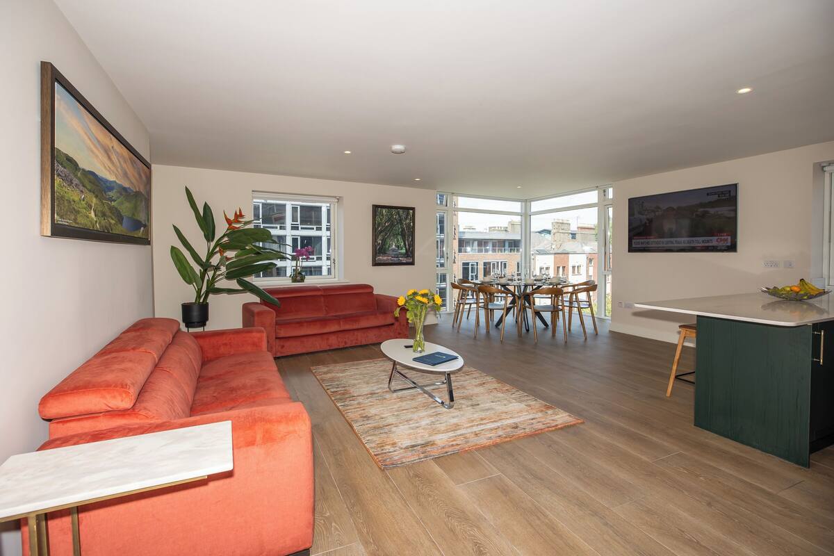 Un salon moderne avec un canapé rouge, une petite table blanche et une plante en pot. On aperçoit à l’arrière-plan un coin repas avec une table et des chaises.