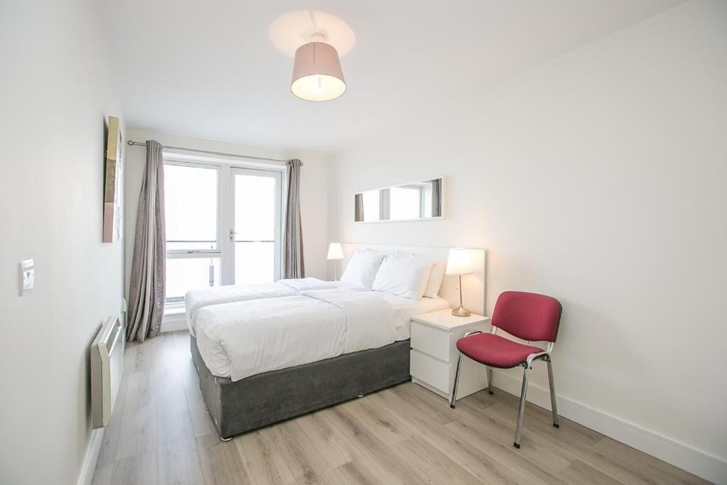 Une chambre d’hôtel moderne équipée d’un lit, d’une table de chevet, d’une chaise et d’une fenêtre avec des rideaux.