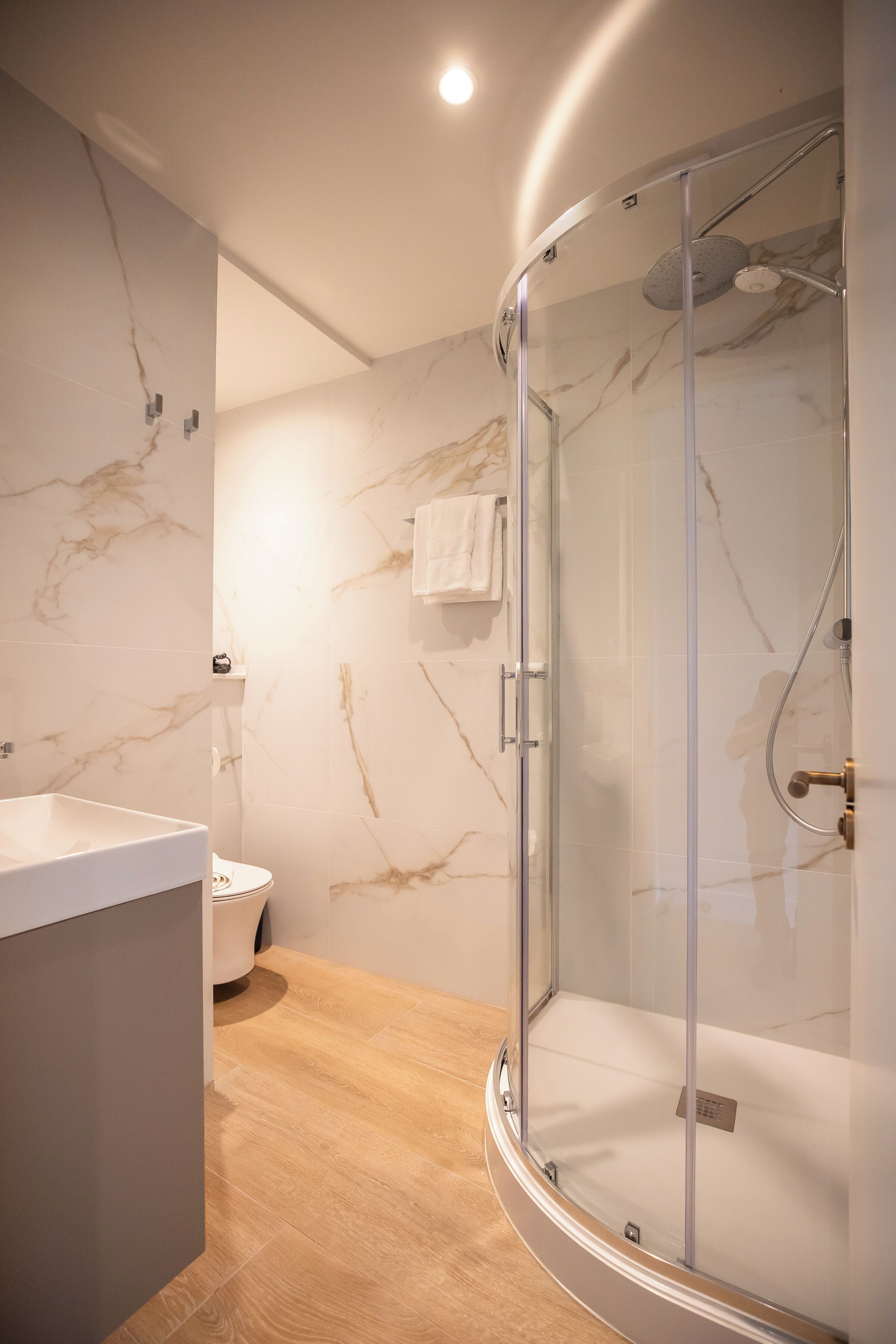 Un bagno moderno con cabina doccia in vetro, pareti in marmo e pavimento in legno.