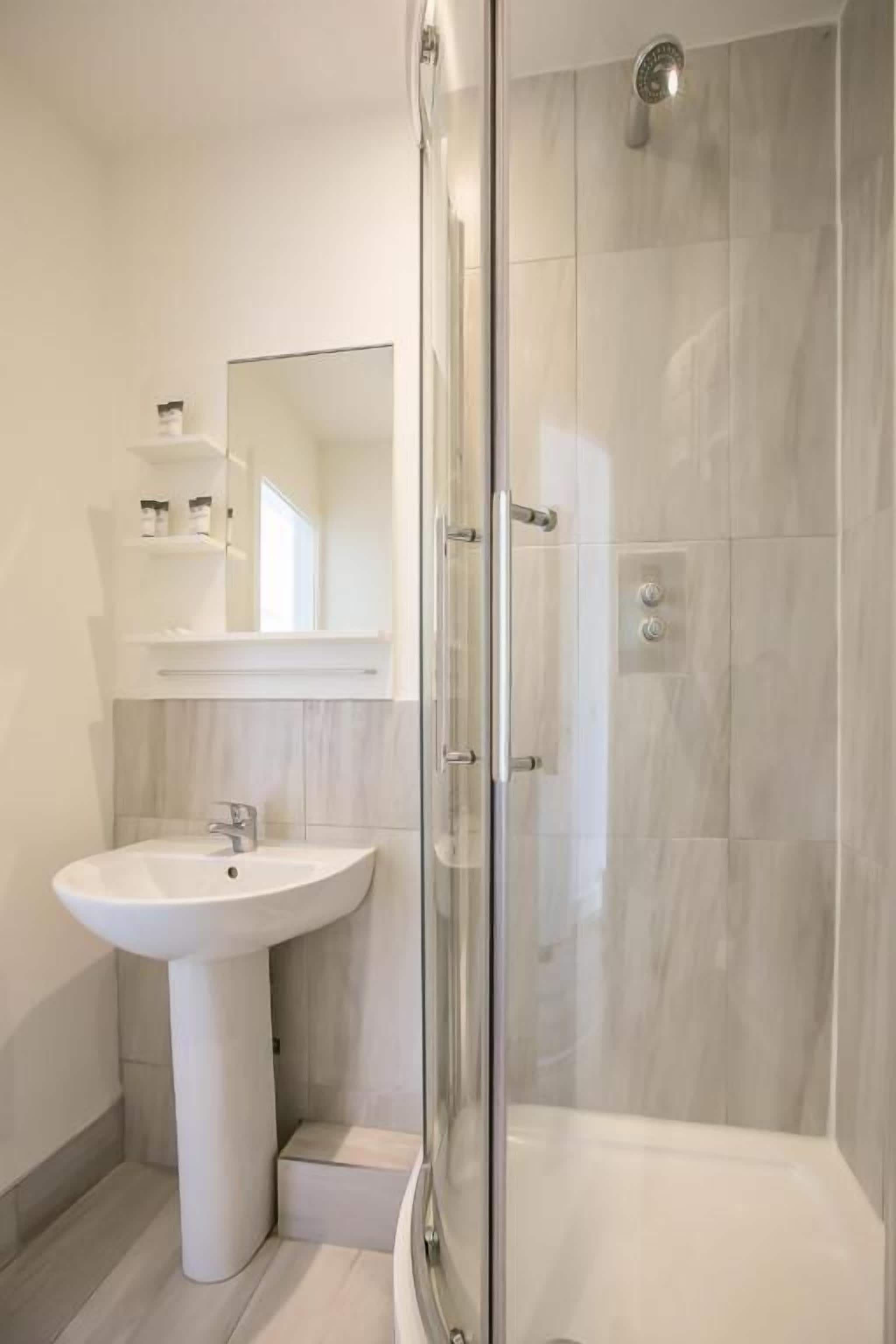 Une salle de bain moderne avec un lavabo sur colonne, une cabine de douche en verre et un miroir au-dessus du lavabo.