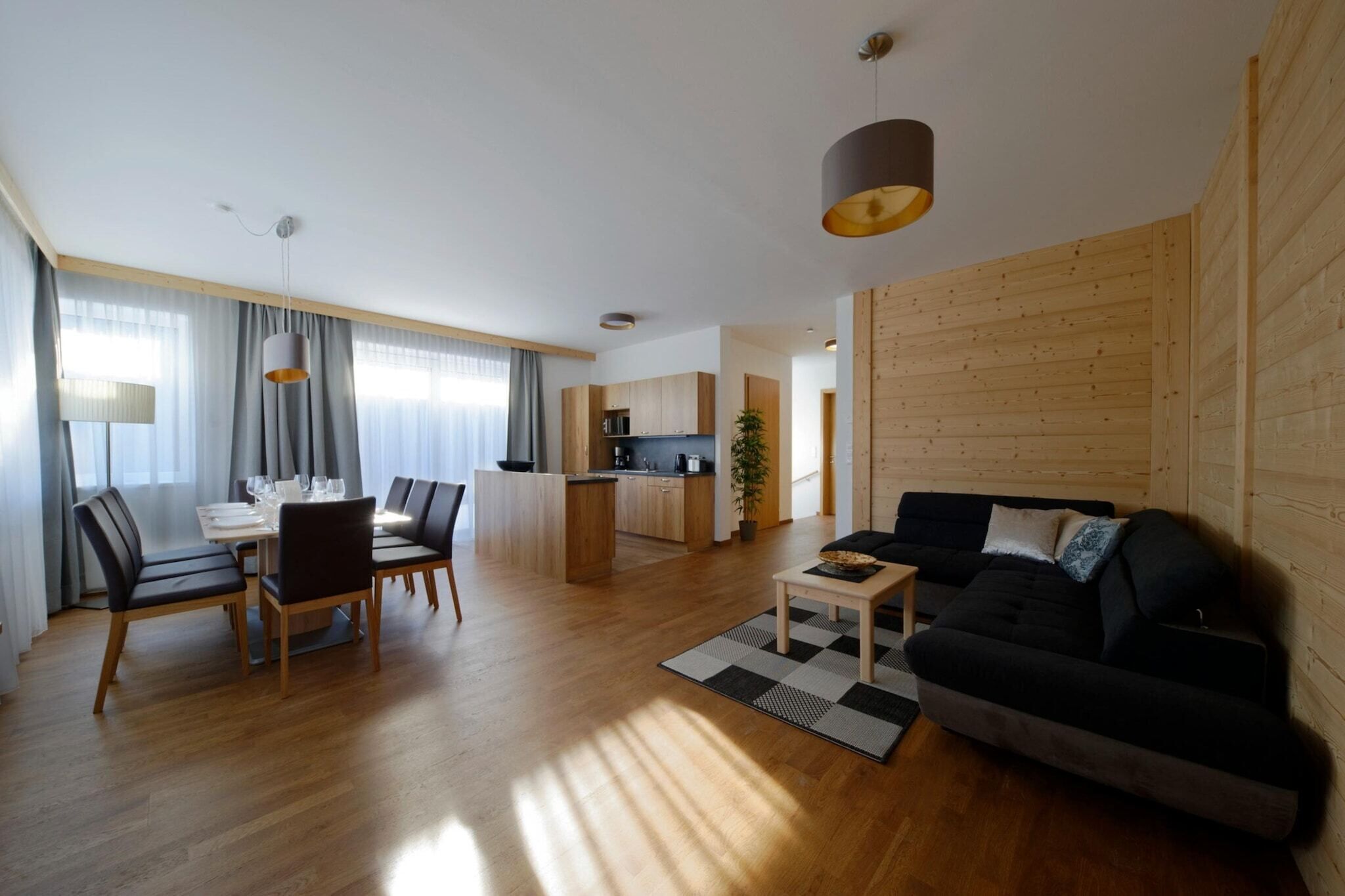 Ein modernes Wohnzimmer mit Sofa, Esstisch und Stühlen. Es gibt eine Küchenzeile mit Holzschränken sowie einen Essbereich mit Tisch und Stühlen.