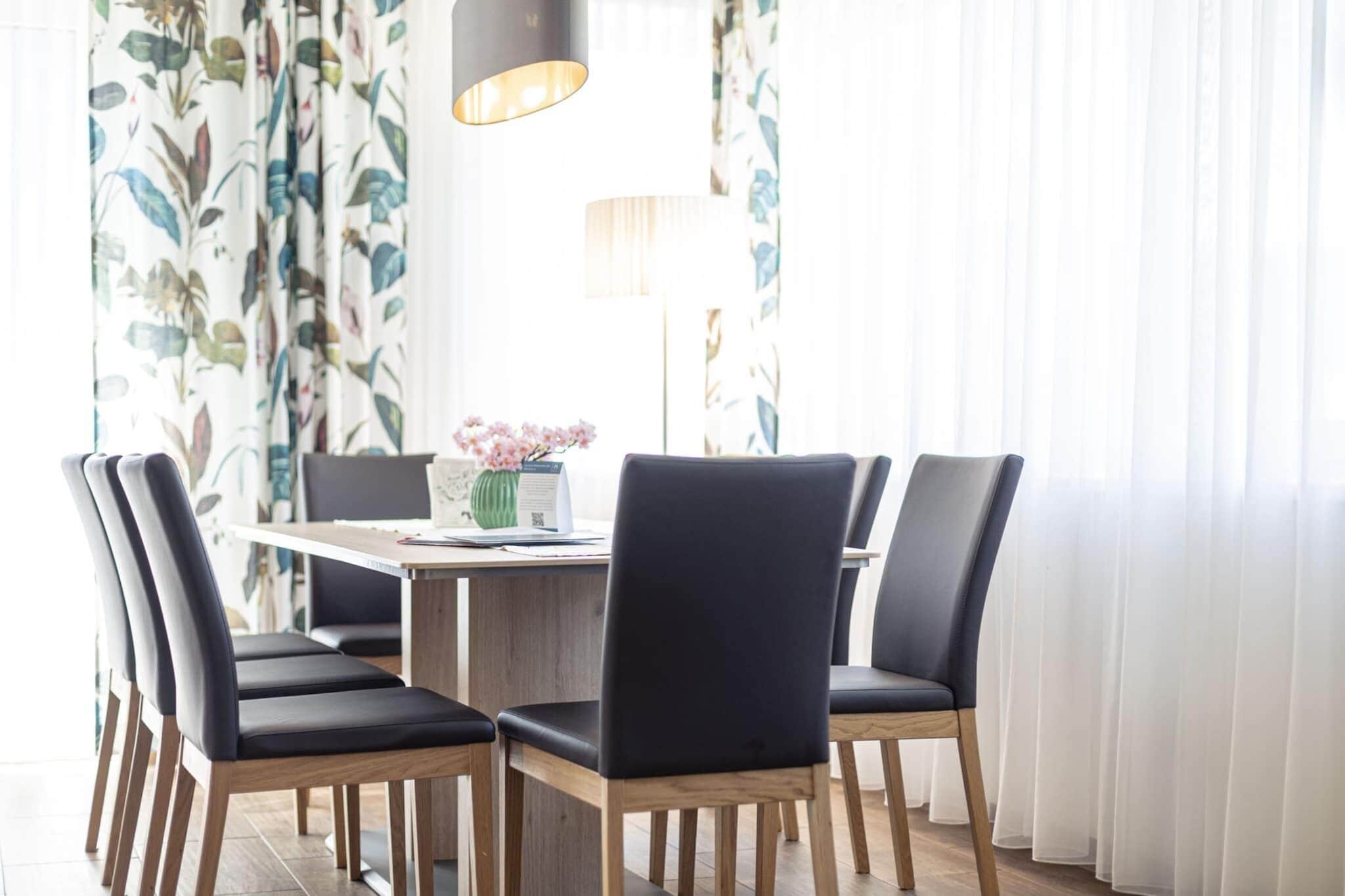 A dining area with a wooden table, black chairs, a vase of flowers, and a lamp.