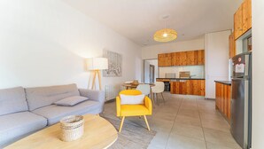 A modern living room with a grey sofa, a yellow armchair, and a wooden coffee table. There is a kitchen area with wooden cabinets and a stainless steel refrigerator. - DOMAINE DU FLAMAND - Gite DUNE  (Naujac-sur-Mer)