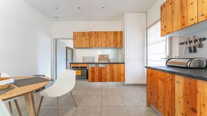 A modern kitchen with wooden cabinets, a dining area with a table and chairs, and a built-in oven. - DOMAINE DU FLAMAND - Gite DUNE  (Naujac-sur-Mer)
