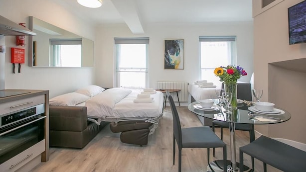 A modern hotel room with a bed, a dining table with chairs, a small kitchenette, and a large window. - St Stephen's Green District-1 (Dublin)