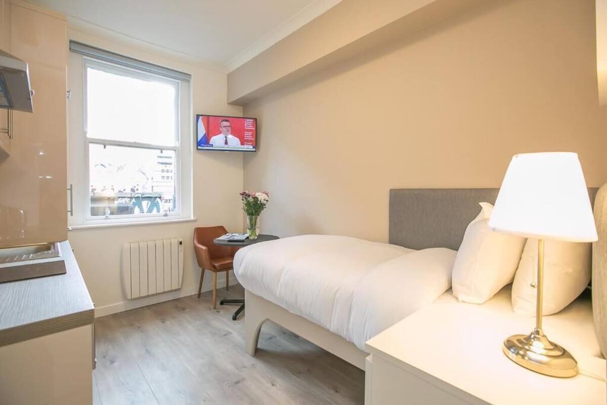A hotel room with a bed, a desk, a chair, a TV mounted on the wall, and a window with a view of the outside.