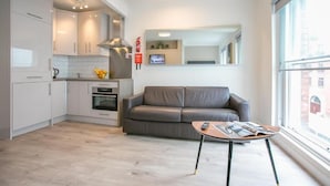 A modern kitchen with white cabinets, a grey sofa, and a small table with a magazine. - St Stephen's Green District-1 (Dublin)
