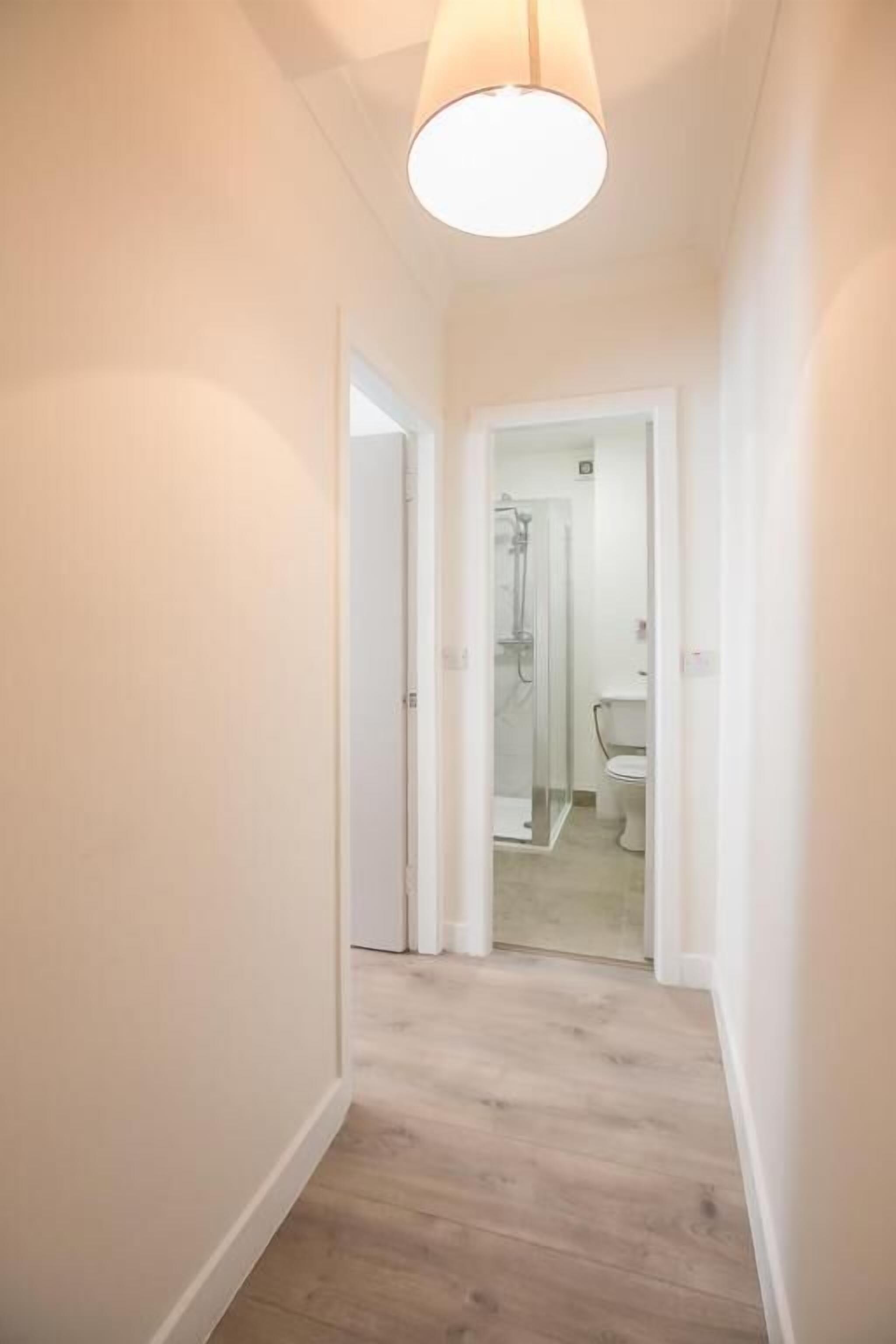 A narrow hallway with wooden flooring and white walls.