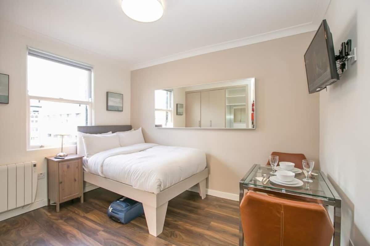 A bedroom with a bed, bedside table, dresser, and a small table with glasses and a cup.