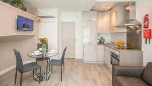 A modern kitchen with white cabinets, a built-in oven, and a sink. There's a dining area with a glass table and chairs, and a television mounted on the wall. - St Stephen's Green District-1 (Dublin)