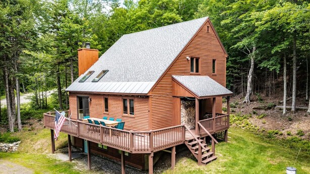 A wooden cabin with a deck, a covered porch, and a staircase leading to an upper level.