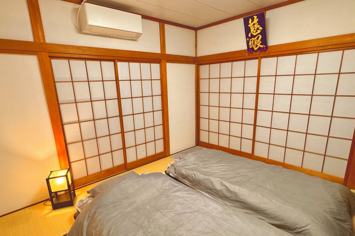 A traditional Japanese room with tatami flooring, a futon bed, a shoji screen, and a small table with a lamp.