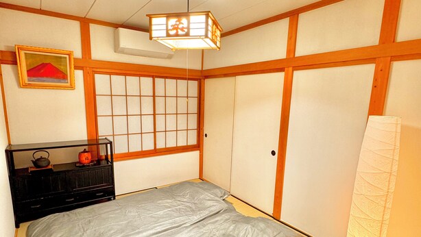 Una camera da letto tradizionale giapponese con pavimento in tatami, un letto futon, un paravento shoji e una lanterna sospesa.