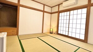 Una stanza tradizionale giapponese con pavimento in tatami, un futon, un paravento shoji e un piccolo tavolo con una lampada.