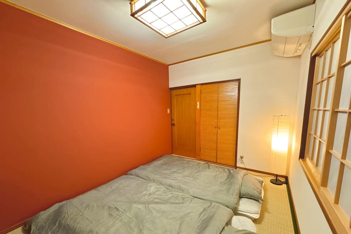 A room with a bed, a wardrobe, a window with a curtain, and a wall-mounted air conditioner.