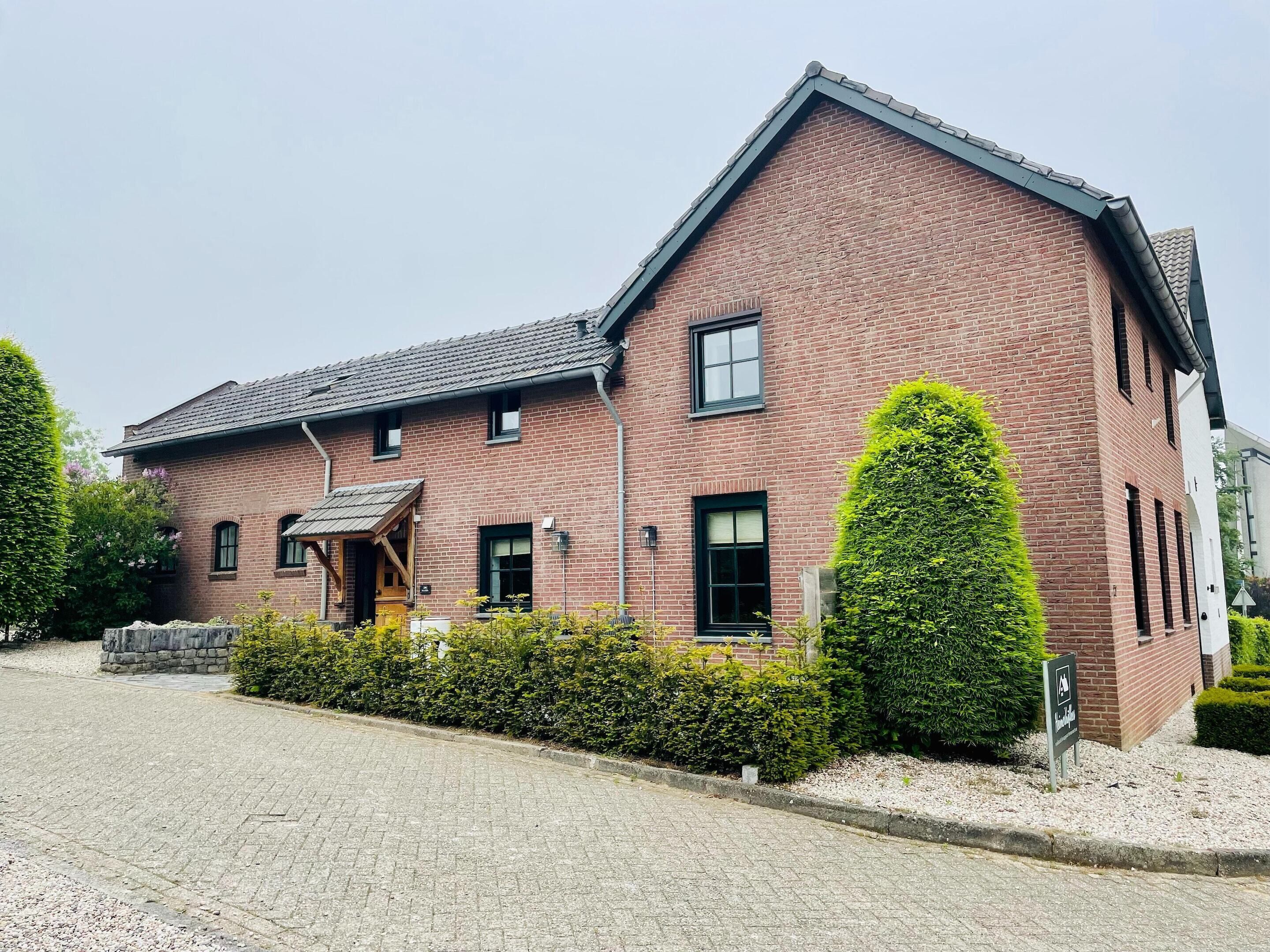 A brick building with a sloped roof, a small porch, and a well-maintained hedge.