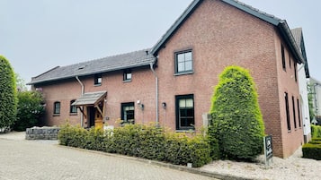 A brick building with a sloped roof, a small porch, and a well-maintained hedge.