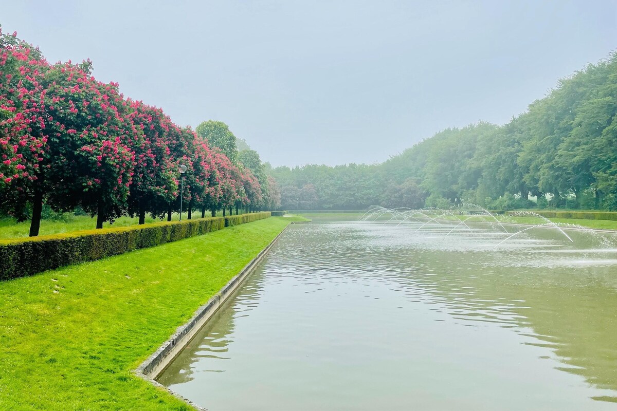 A serene park with a water canal, neatly trimmed hedges, and flowering trees.