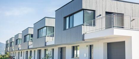 A modern multi-story hotel with a flat roof, large windows, and a covered outdoor area with a metal railing.