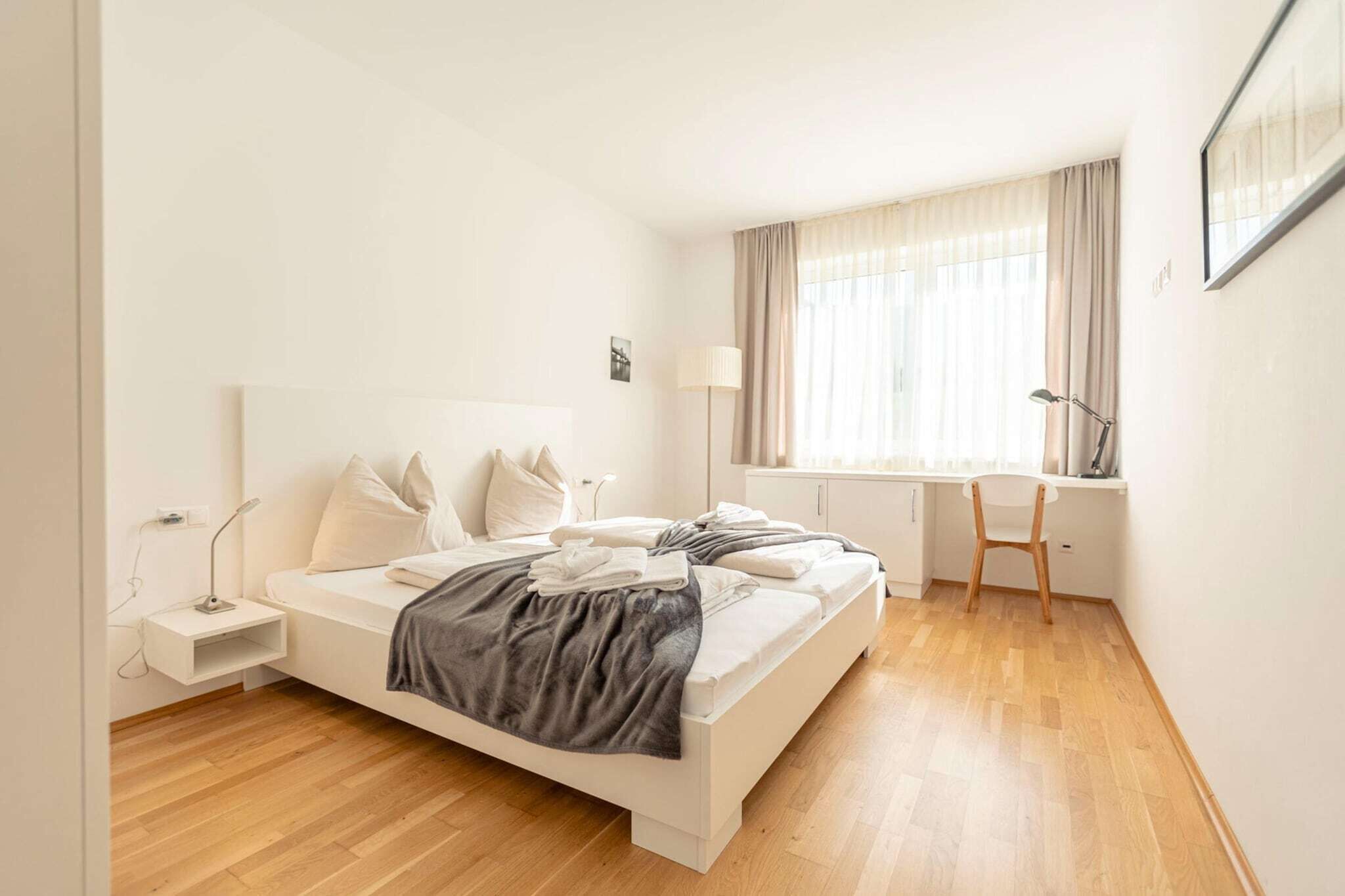 Ein modernes Schlafzimmer mit Bett, Nachttisch, Lampe und Schreibtisch mit Stuhl.